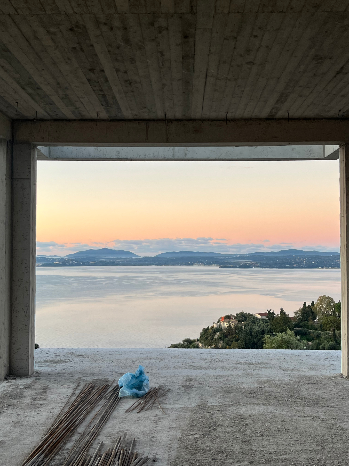 Concrete shell of a new Corfu villa framing a pastel sunset over the sea